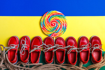 A lot of small red boat shoes near big multi-colored lollipop on colored background.  Top view, copy space. Frame. group of child boat shoes.