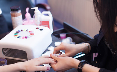 Closeup shot of a woman in a nail salon receiving a manicure by a beautician with nail file. Woman getting nail manicure. Beautician file nails to a customer. Blurred background