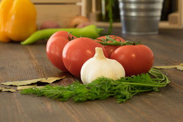 Tomato, garlic and greens on the dark wood with other vegetables in blurred background