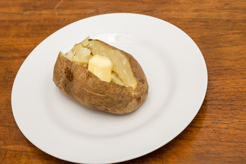 Hot Buttered Potato on White Plate and Wood Table