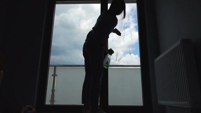 Silhouette of young woman cleaning a window at her home, 4K
