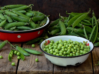 Green pea pods and cleaned in a metal bowl on a wooden background