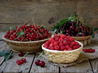 Fresh fruit and berries in baskets on wooden background - currants, raspberries, cherries