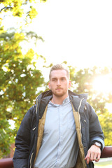 Obraz premium An attractive blonde man standing leaning outdoors on a sunny day with the sun right behind him, lens flare. Looking away from camera.