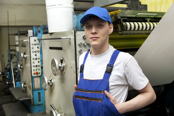 Young man in cap working on offset printing machine