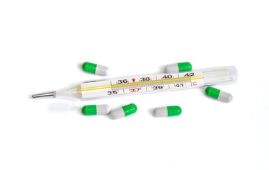Medicine pills or capsules and thermometer on white background.