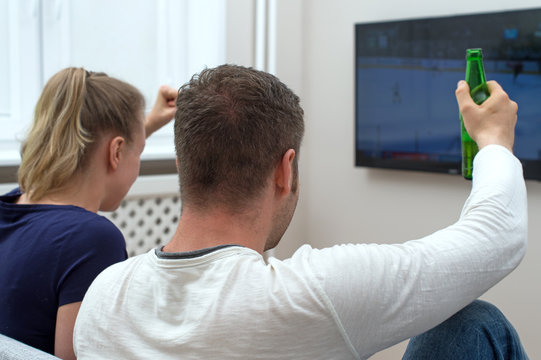 Excited couple watching hockey match on tv.