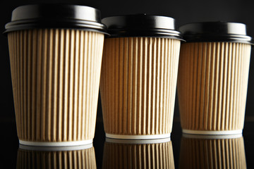 Luxury set of brown take away cardboard paper cups closed with caps isolated on black and mirrored. Retail mockup presentation