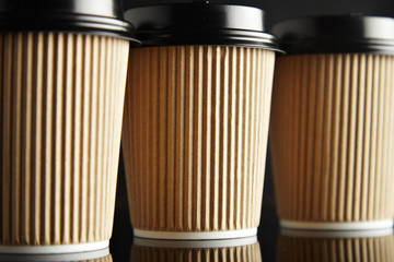 Closeup of rustic take away cardboard paper cups closed with caps isolated on black and mirrored. Retail mockup presentation