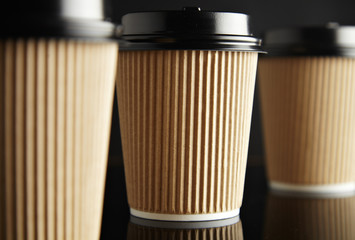 Three brown take away cardboard paper cups closed with caps isolated on black and mirrored. Retail mockup presentation