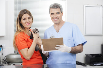 Obraz premium Male Vet Holding Clipboard By Woman With Weasel