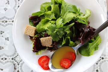 Green salad with strawberry pieces and a dressing of orange juic