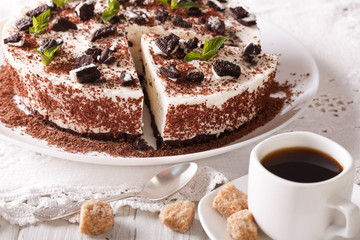 Cut cheese cake with pieces of chocolate cookies and coffee on the table. horizontal
