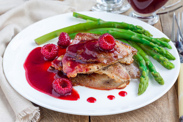 Pork cutlets with raspberry sauce and asparagus on white plate
