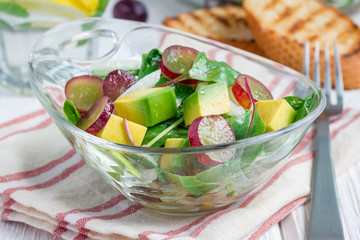 Vegetarian salad with avocado, grape, rucola, onion, in glass bowl