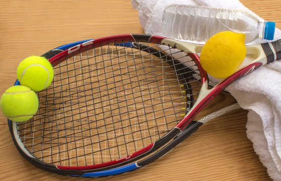 Tennis rackets and balls are next to a bottle of water and lemo