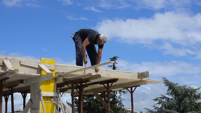 Construction roofer nailing wood board with hammer on roof installation work
