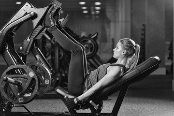 Sportive woman using weights press machine for legs at the gym. Pretty brunette exercising in a...