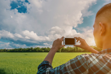 closeup of a young man using a smartphone in a natural landscape, with a meadow in the background - 114377552