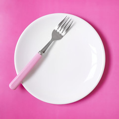 Crockery and plates - a plain white, empty dinner dish with fork on a pink background