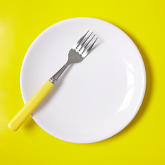 Crockery and plates - a plain white, empty dinner dish with fork on a yellow background