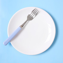 Crockery and plates - a plain white, empty dinner dish with fork on a blue background