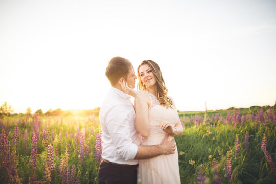 Bride holds groom's neck while he kisses her in the rays of sunset