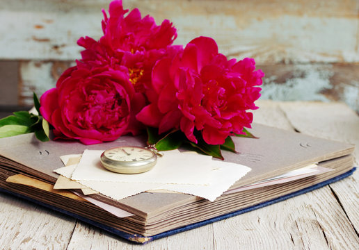 Bouquet of pink peonies, old photo album, old empty photographs and a pocket watch close up