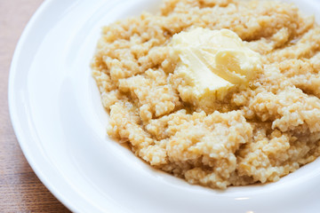 A healthy Breakfast of crushed barley and millet porridge with butter served in a white plate closeup