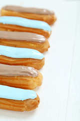 Eclairs with glaze on a white wooden table
