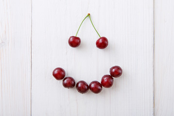 Sweet fresh cherries smile on white wood background