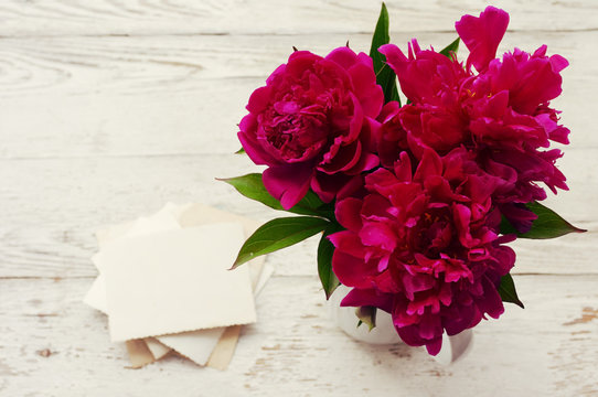 Bouquet of pink peonies in a white jug and old empty photographs close up, top view