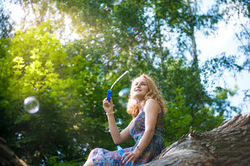 Young teen girl sitting on a tree in the forest playing with soap bubbles