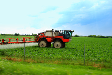 Tractor spraying wheat field with sprayer during sunset