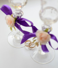 Two glasses with violet bands and roses, and wedding rings on it