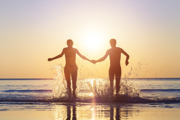 Happy couple running to the sea with splashes of water