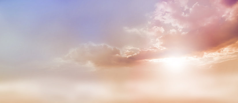 Dreamy Romantic Sky scape - beautiful wide peach and dusky pale blue sky and cloud scape with a burst of sunlight emerging from under the cloud base with plenty of copy space