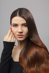 Closeup portrait of beautiful woman with luxurious and gorgeous brown hair posing over grey backhroung. Woman with modern hairstyle in studio.