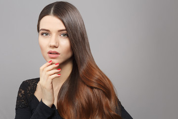 Beautiful woman with gorgeous brown hair posing over grey background. Lady with modern hairstyle looking at camera in studio.
