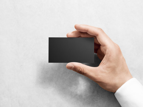 Hand holding blank plain black business card design mockup. Clear calling card mock up template hold arm. Visit pasteboard paper surface display front. Check small offset card print dark business card