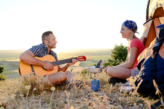 young romantic couple playing guitar in tent camp on summer outdoor adventure hiking trip