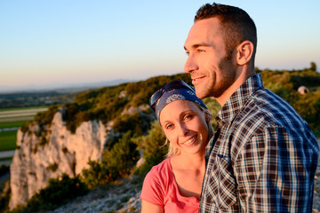 young couple with backpack on adventure mountain trek admiring a beautiful sunset landscape