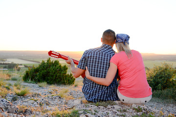 Fototapeta na wymiar romantic couple playing guitar and admiring beautiful sunset landscape