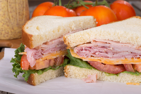 Ham Sandwich Closeup With Mustard and Tomatoes in Background