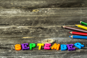 school supplies on wooden background, colorful pencils, with the word September