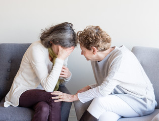 Older mother in cream top comforting middle aged daughter with hand over face