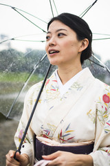 Young attractive Japanese woman in kimono holding an umbrella on a rainy day