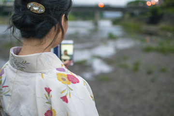 Young attractive Japanese woman in kimono taking selfie with cellphone outside