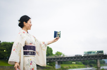 Young attractive Japanese woman in kimono taking selfie with cellphone outside