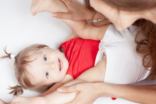 Funny baby girl lying near happy mother on white bed